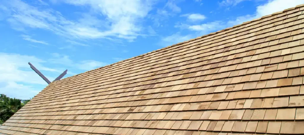 Toiture en bois - Couverture Travaux Une vue rapprochée d'une toiture en bois montre des bardeaux de bois soigneusement alignés, créant un aspect texturé sous un ciel bleu vif avec des nuages épars.